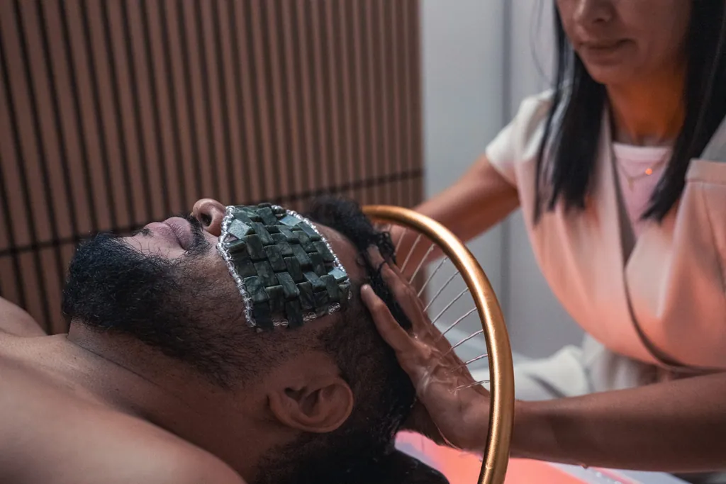 Ritual de Head Spa, com uma pessoa deitada, pedras sobre os olhos e um arco de cobre
