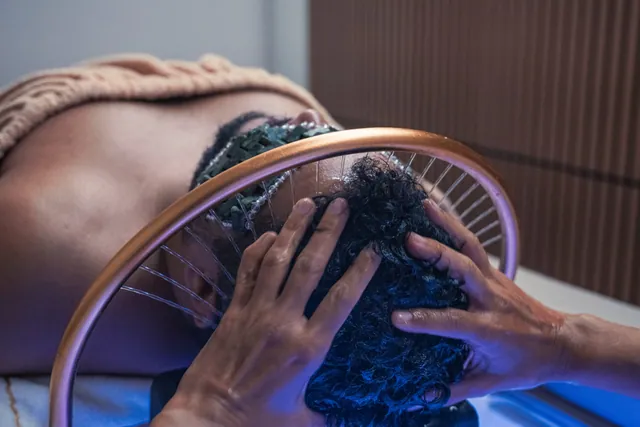 Pessoa deitada durante um ritual de Head Spa, com pedras sobre os olhos e um arco dourado sobre a cabeça
