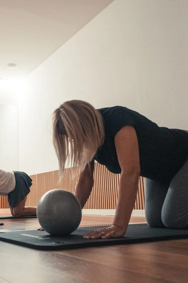 Aluna em exercício de pilates com bola, de joelhos sobre o tapete